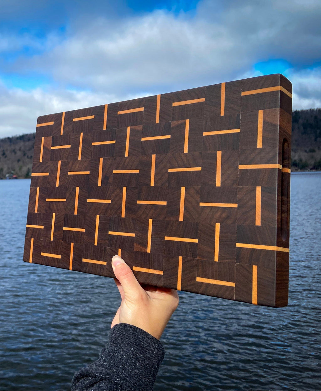Wooden cutting board with geometric pattern held over a lake
