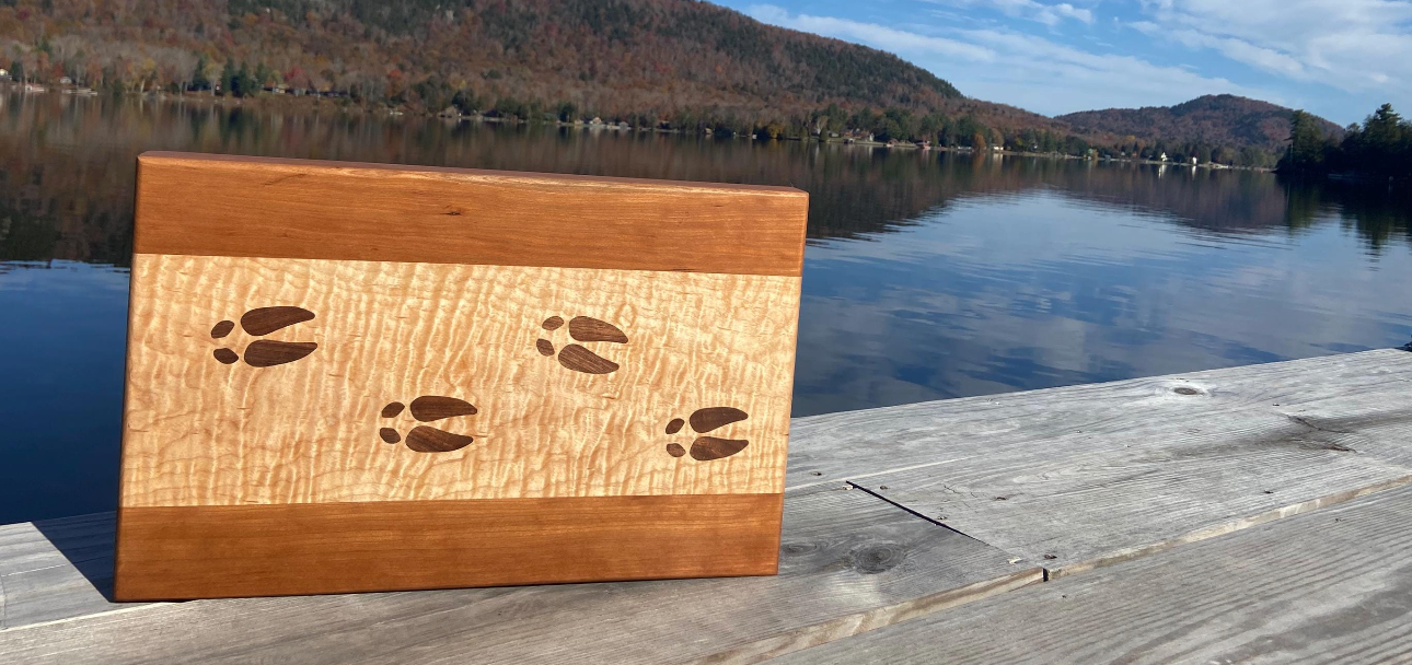 Wooden sign with paw prints on a dock by a lake with mountains in the background